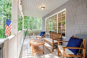 A covered porch with wooden furniture and a view of a forest. - Dreamy Retreat in the Woods with Firepit, Fireplace, Free and Large Deck (Eastsound)