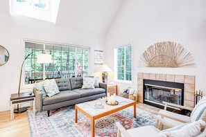 A living room with a sofa, coffee table, fireplace, and large windows. - Dreamy Retreat in the Woods with Firepit, Fireplace, Free and Large Deck (Eastsound)