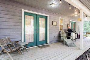 En veranda av trä med en grön dörr, en bänk och ett litet bord med en stol.