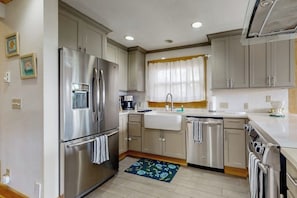 A kitchen with stainless steel appliances, a sink, and a window with curtains. - Stunning Oceanfront Getaway in Langley with Private Patio and WiFi (Langley)
