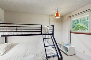 A bunk bed room with a ladder, a small white table with books, and a window with blinds.