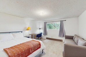 Ein Hotelzimmer mit Bett, Schreibtisch, Stuhl, einer Couch und einem Fenster mit Vorhängen.