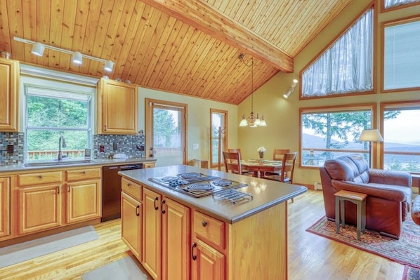 A spacious kitchen with wooden cabinets, a central island, and large windows. - Updated Eastsound Home with Stunning Mountain and Ocean Views (Eastsound)