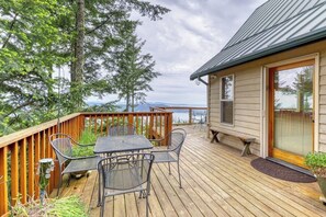 A wooden deck with a table and chairs, overlooking a body of water and trees.