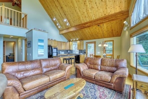 A spacious living area with leather sofas, a wooden coffee table, and a view of the kitchen and outdoors. - Updated Eastsound Home with Stunning Mountain and Ocean Views (Eastsound)