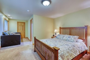 A bedroom with a bed, a nightstand, a lamp, a sofa, and a door. - Updated Eastsound Home with Stunning Mountain and Ocean Views (Eastsound)