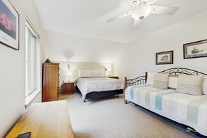 A bedroom with two beds, a wooden nightstand, a desk, and a ceiling fan.