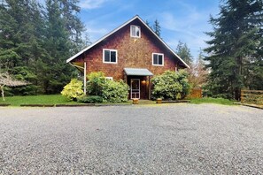 Una casa a due piani in legno con vialetto sterrato e giardino recintato.
