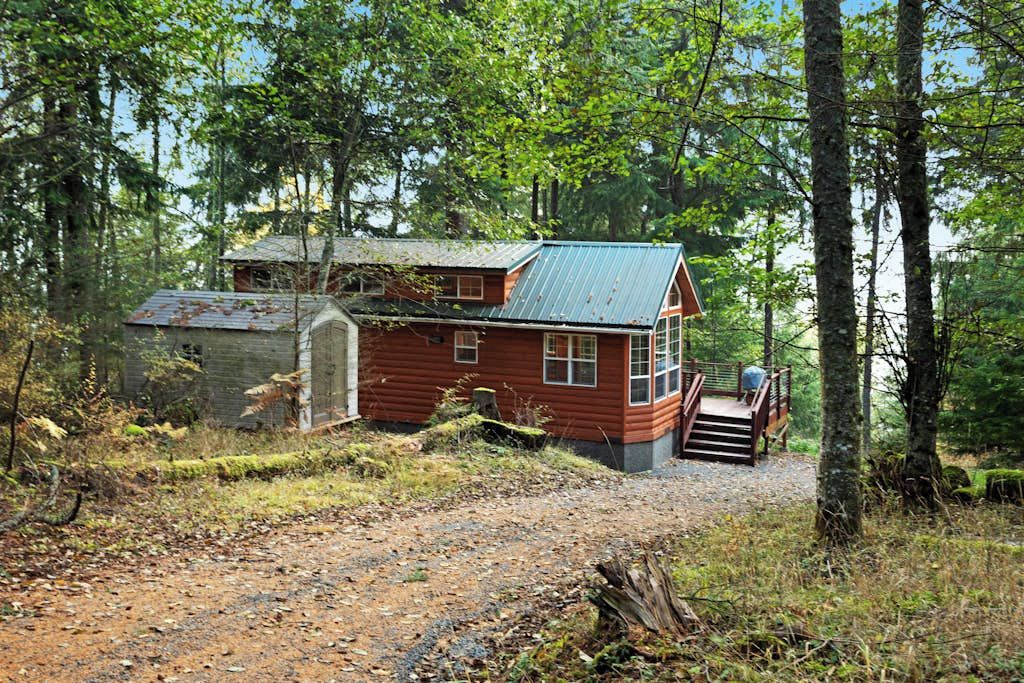 Une cabane avec un toit en métal, une terrasse en bois et un chemin de gravier menant à l’entrée.