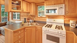 A compact kitchen with wooden cabinets, a gas stove, a microwave, and a sink. - Cozy 1BR Waterfront Cabin with Mountain Views (Eastsound)