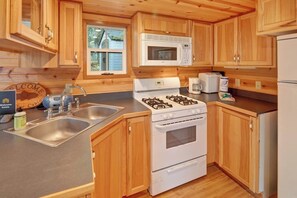 A cabin-style kitchen with wooden cabinets, a gas stove, a microwave, and a sink.