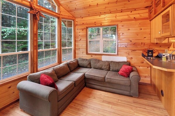 A cabin interior with a sectional sofa, wooden walls, and large windows.
