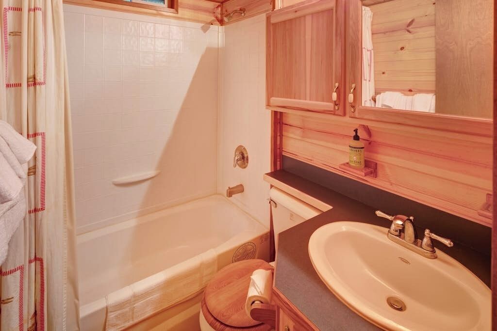 Une salle de bain avec une baignoire, un abattant de toilettes en bois, un lavabo et un miroir.