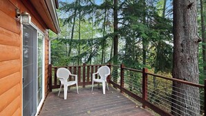 A wooden deck with two white chairs, a railing, and a view of a forest. - Cozy 1BR Waterfront Cabin with Mountain Views (Eastsound)