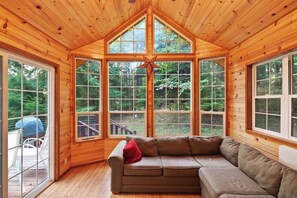 A cabin interior with a wooden ceiling, a large window, and a brown sofa.