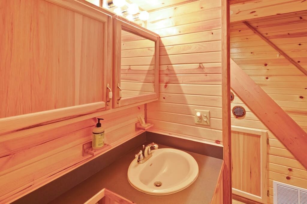 A wooden cabin interior with a bathroom featuring a sink, mirror, and wooden cabinets.