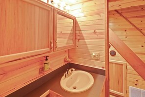 A wooden cabin interior with a bathroom featuring a sink, mirror, and wooden cabinets.