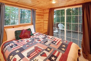 A wooden cabin bedroom with a large bed, a window with curtains, and a view of the outdoors.