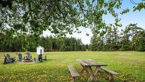 Eine Außenansicht mit Picknicktisch und Stühlen, einem kleinen Schuppen und einer Feuerstelle.
