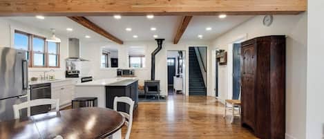 A modern kitchen with wooden beams, a dining area, and a staircase leading to another level.