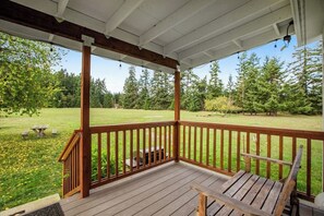 A wooden deck with a railing, a bench, and a grill in the background.
