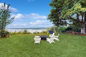A grassy outdoor area with a swing set, two white chairs, and a round table.