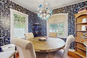 A dining area with a round table, four chairs, a chandelier, and a bookshelf. - Whimsical 1940s Waterview Gem with Sweeping sea views, Wildlife, & Near Town (Langley)