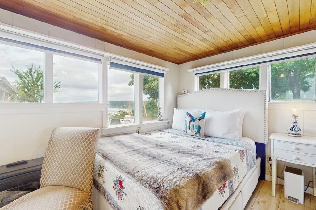 A bedroom with a large bed, a chair, a desk, and a window with a view of trees.