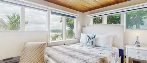 A bedroom with a large bed, a chair, a desk, and a window with a view of trees.