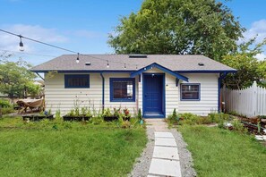 A single-story house with a blue front door, a small porch, and a garden with various plants. - Whimsical 1940s Waterview Gem with Sweeping sea views, Wildlife, & Near Town (Langley)