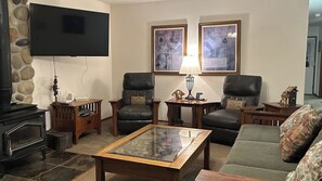A living room with a fireplace, leather armchairs, a glass-top coffee table, and artwork on the walls. - Waterfront Cabin with Hot Tub and Mountain Views in Eastsound (Eastsound)
