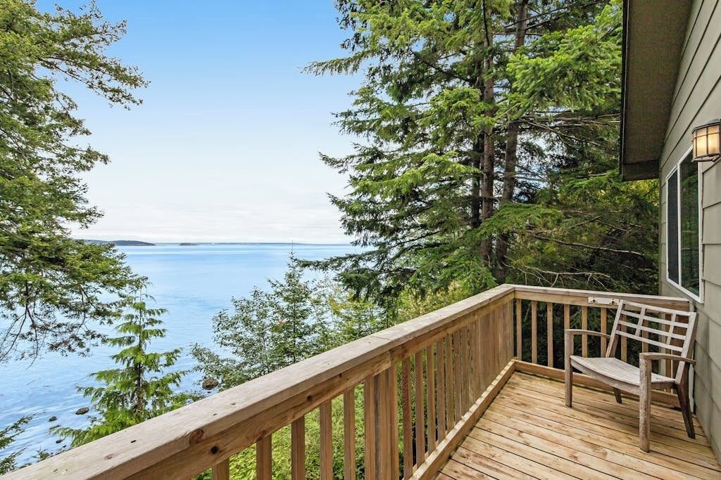 A wooden deck with a bench overlooking a body of water and dense forest.
