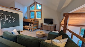 A cozy room with a bunk bed, a television, a round coffee table, and a large window.