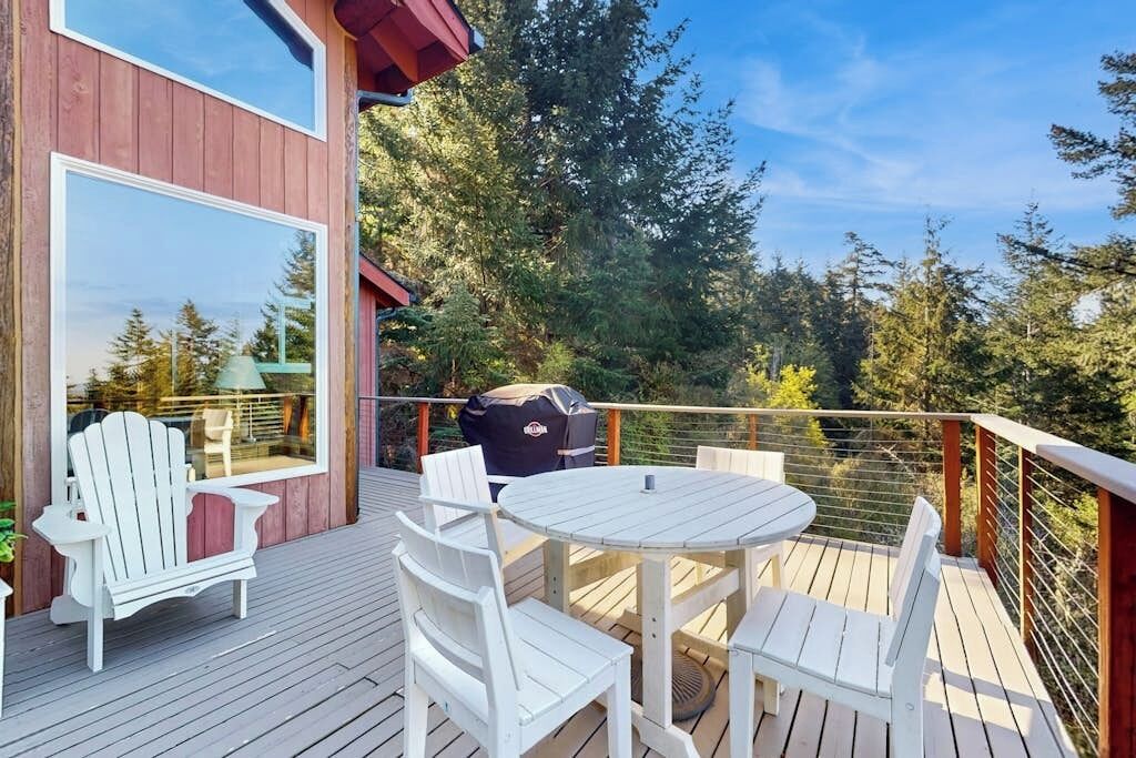 A wooden deck with outdoor furniture, a grill, and a view of trees.