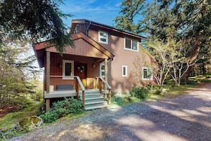 A two-story wooden house with a front porch and a gravel driveway.