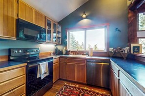 A modern kitchen with wooden cabinets, a stainless steel dishwasher, and a large window providing natural light. - Beautiful Secluded Cabin with Stunning Bay Views and Private Deck (Eastsound)