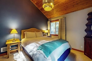 A bedroom with a wooden ceiling, a bed with a headboard, two bedside lamps, a window with curtains, and a nightstand. - Beautiful Secluded Cabin with Stunning Bay Views and Private Deck (Eastsound)