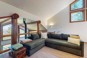 A cozy living room with a sectional sofa, a wooden chest, and a view through large windows.