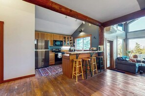 A modern kitchen with wooden cabinets, a central island with stools, and a large window providing natural light. - Beautiful Secluded Cabin with Stunning Bay Views and Private Deck (Eastsound)