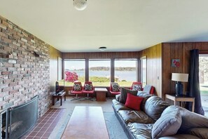 A living room with a fireplace, a sofa, a coffee table, and a view of a lake.