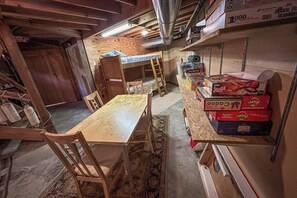 A room with a wooden table and chairs, a bunk bed, and shelves with various items including boxes and a water dispenser.
