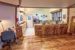 A kitchen with a central island, bar stools, wooden flooring, and a visible door leading to another room.