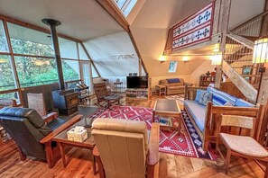 A cozy, well-lit living room with a fireplace, comfortable seating, and a large window offering a view of the outdoors.