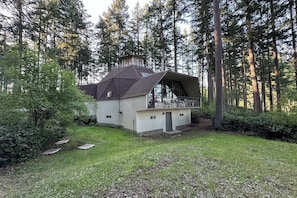 A modern house with a sloped roof, large windows, and a balcony overlooking a forested area.