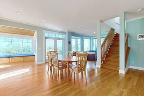 A spacious dining area with a wooden table and chairs, a staircase, and large windows.