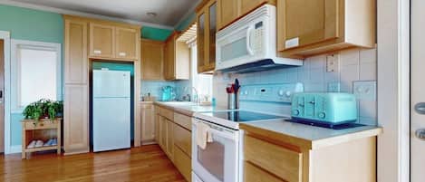 Una cocina con armarios de madera, un refrigerador blanco, un microondas, una estufa y un tostador.