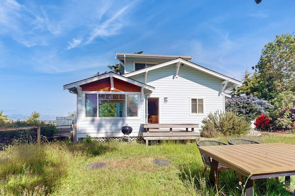 Ein zweistöckiges Haus mit Veranda, einer Holzterrasse und Blick auf den Ozean.
