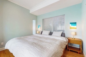 Un dormitorio con una cama grande, una mesita de noche, una ventana con persianas y una lámpara de pared.