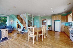 A spacious living area with a wooden dining table and chairs, a staircase, and a kitchen with wooden cabinets and a refrigerator.