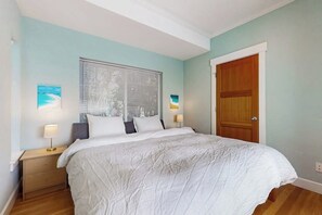 Quarto com cama, duas mesas de cabeceira, janela com persianas e porta.